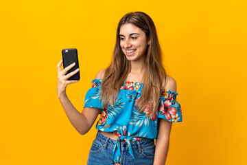 Young woman using mobile phone over isolated yellow background with happy expression