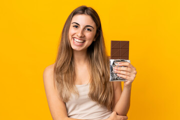 Young woman over isolated yellow background taking a chocolate tablet and happy