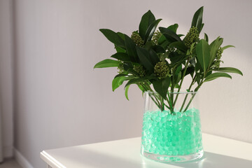 Mint filler with green branches in glass vase on white table, space for text. Water beads
