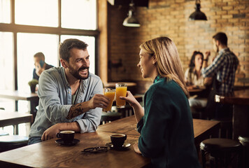 Young happy couple toasting with orange juice in a cafe.