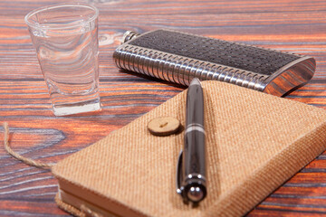 Notepad, pen, glass and flask on the wooden table