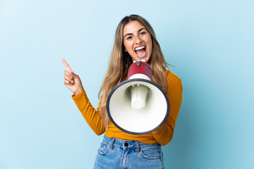 Young hispanic woman over isolated blue background shouting through a megaphone and pointing side