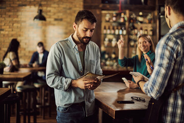 Young man reading menu while making order in a pub.