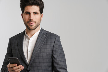 Confident young man in jacket posing and using mobile phone