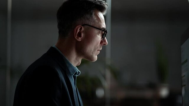 A side view of a handsome businessman is working using his computer in the office in the evening