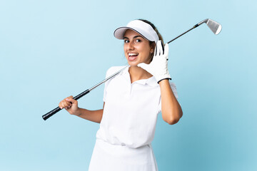 Young hispanic golfer woman over isolated blue wall listening to something by putting hand on the...