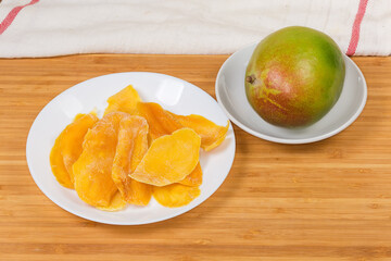 Dried mango slices and fresh whole mango on a wooden surface