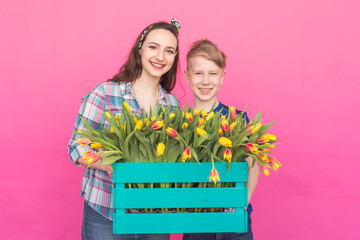 Family portrait sister and teenager brother with tulips on pink background