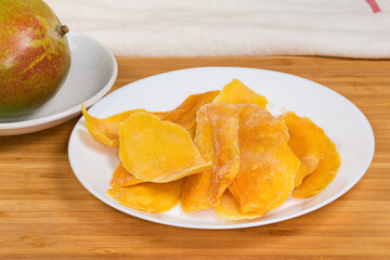 Dried mango slices against fresh whole mango on a wooden surface
