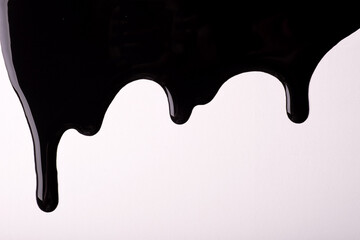 Black liquid drops of paint color flow down on isolated white background. Abstract dark backdrop...