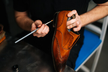 Close-up top view of shoemaker painting heel and sole of light brown leather shoes with brush during restoration working. Concept of cobbler artisan repairing and restoration work in shoe repair shop.