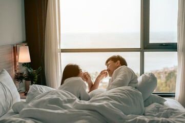 Asian couple is talking and smiling on the bed in bed room at modern home,Young couple pointing to the nose of each other..Couple in Valentine day.Love couple,Relationship and couple concept.