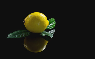 Fresh yellow lemon with green leaves and reflection on a black isolated background. Close-up, copy space