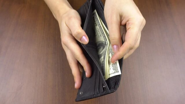 Women's hands hold a wallet and count dollars in it.women's hand taking cash from a man's wallet.