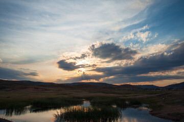 Sunset over a small lake and village in the valley amongst rocky terrain in the Bayanaul National Park, Kazakh Uplands.