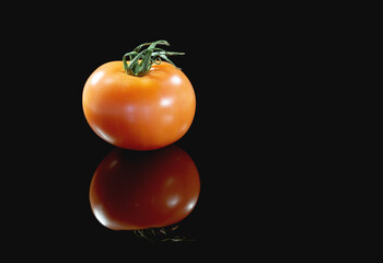 A large red tomato with a reflection on a black isolated background. Close-up, copy space