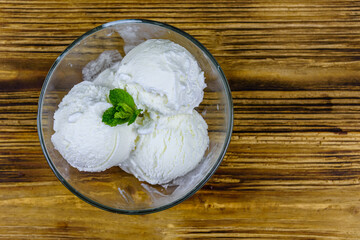 Glass bowl with ice cream balls and mint leaf on a wooden table. Top view