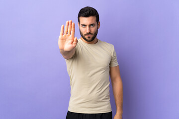 Young handsome man with beard over isolated background making stop gesture