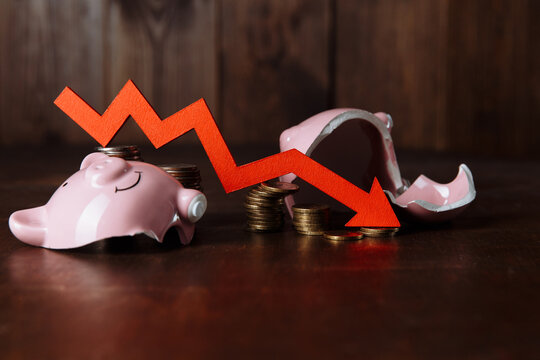 Broken piggy bank and red arrow on coins stack. Investment and crisis concept