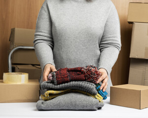 woman in a gray sweater collects clothes in a box, concept of assistance and volunteering, moving
