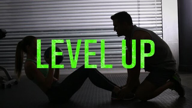 Animation of level up text in green letters over woman doing crunches with male instructor