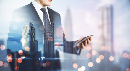 Freelance mobile working concept with man in black suit looking at digital tablet on blurry megapolis city background