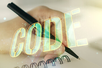 Creative Code word hologram and man hand writing in notepad on background, artificial intelligence and neural networks concept. Multiexposure