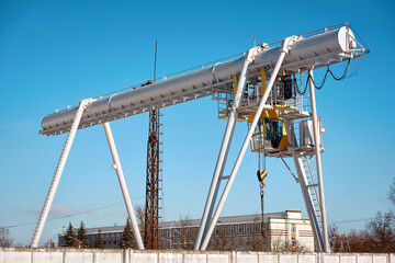 Gantry crane with hook, lifting and carrying heavy cargo against blue sky background. Huge overhead crane on industrial site
