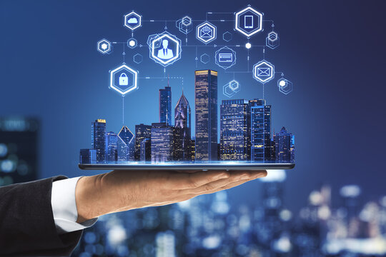 Internet of things in smart city concept with businessman hand holds digital tablet with night skyscrapers