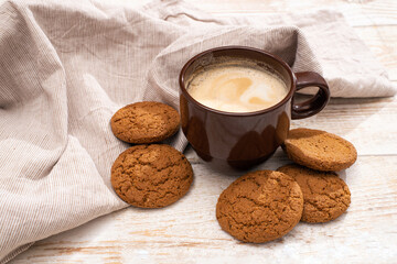 A cup of aromatic coffee cappuccino with Oatmeal cookies. Morning rays and latte for breakfast in a beautiful brown cup. Wooden background.