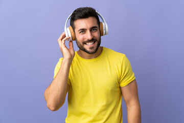 Young handsome man with beard isolated on purple background listening music
