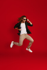 Full length of happy young man in casual clothing smiling and gesturing while hovering against red background