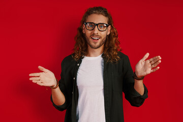 Happy young man in casual clothing looking at camera and smiling while standing against red background