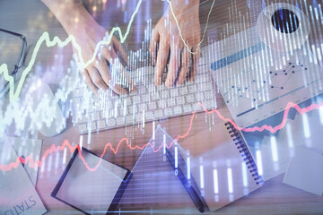 Multi exposure of man's hands typing over computer keyboard and forex graph hologram drawing. Top...