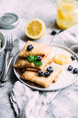 Crepes with homemade cottage cheese, blueberries and lemon curd on a gray plate