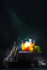 Whiskey or cognac in glass, with lime, ice cubes ans barmen utensils, dark background with on stand pedestal copy space