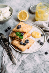 Crepes with homemade cottage cheese, blueberries and lemon curd on a gray plate