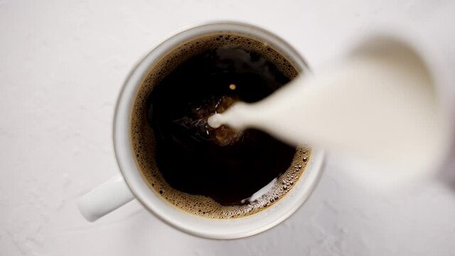 Adding cream to a cup with black, hot coffee placed on white table