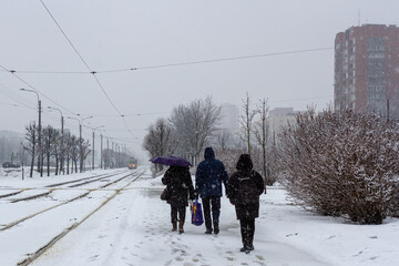 People on the city street. Three persons. Woman with an umbrella. A tram in the distance. Spring snowfall in the Russian city of St. Petersburg, residential district.