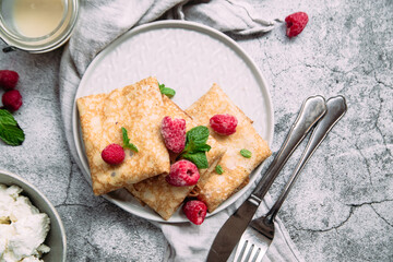 Crepes with homemade cottage cheese, raspberries a gray plate