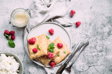 Crepes with homemade cottage cheese, raspberries a gray plate
