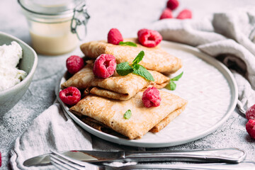 Crepes with homemade cottage cheese, raspberries a gray plate