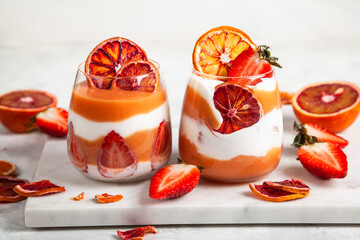 Layered trifle dessert with blood oranges cream Kurd, greek yogurt, Savoyardi cookies, orange chips and strawberry in serving glasses.