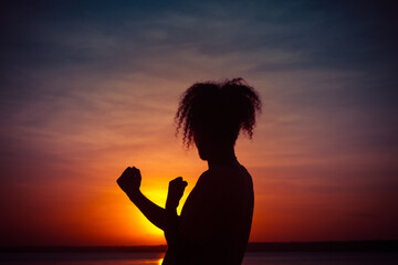 Silhouette of a young man with arms raised during sunset. sign of joy or victory. Curly hair on a man.