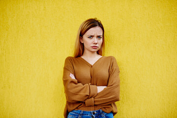 Serious woman with folded hands near yellow wall