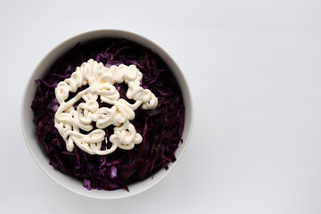 Easy homecooked creamy coleslaw from red cabbage in a bowl on white table background. Top view, copy space. Fresh vegetable salad with mayonnaise dressing. Flat lay food. Healthy eating concept
