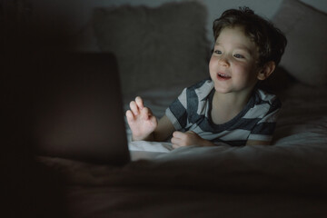 Little boy using laptop by night at home on the bedroom.