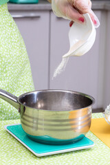 The process of pouring sugar from a saucer into a saucepan to make syrup. Selective focus.