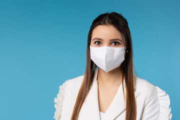 Portrait of a young serious lady in a white protective mask on a blue background looks at the camera. Office work and business during a pandemic.