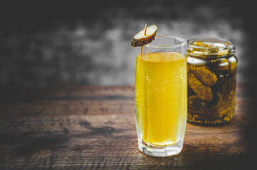 Pickle juice in glass and a can of pickled cucumbers on wooden table background